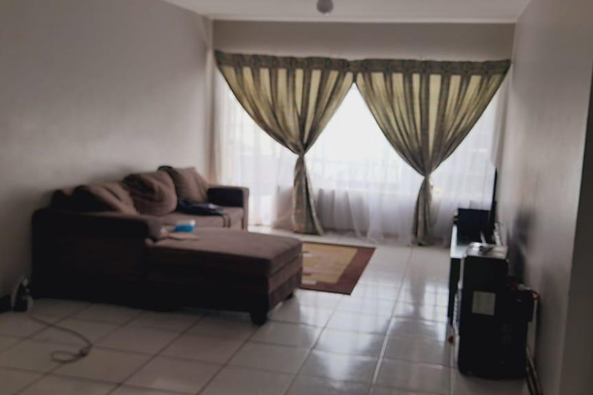 A living room area featuring tiled flooring and a large window with curtains, providing natural light to the space.