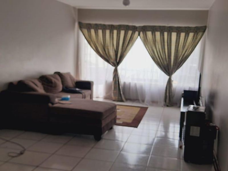 A living room area featuring tiled flooring and a large window with curtains, providing natural light to the space.