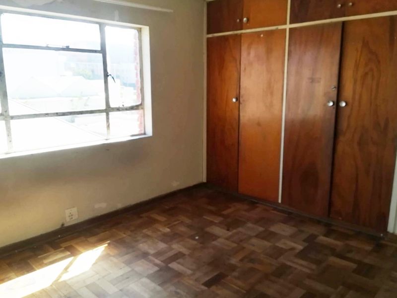 An empty bedroom featuring original parquet flooring, built-in wooden cupboards, and a steel-framed window, offering a blank canvas for renovation.