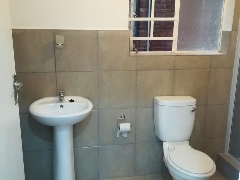 A functional bathroom featuring a pedestal basin, toilet, and neutral wall and floor tiling with a window providing natural light.