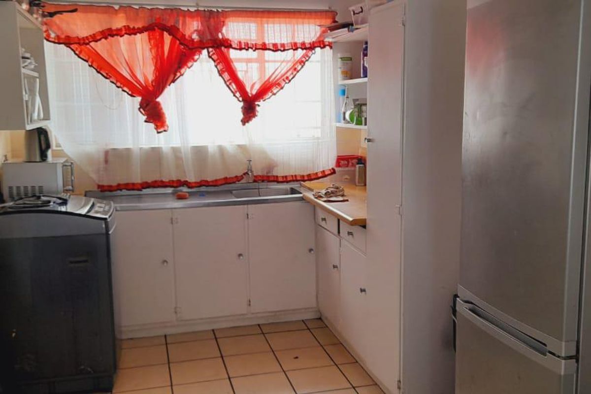 A functional kitchen featuring built-in cabinetry, a stainless steel sink, and tiled flooring, offering a practical layout with potential for modern updates.