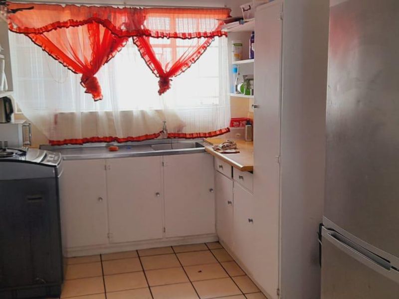 A functional kitchen featuring built-in cabinetry, a stainless steel sink, and tiled flooring, offering a practical layout with potential for modern updates.
