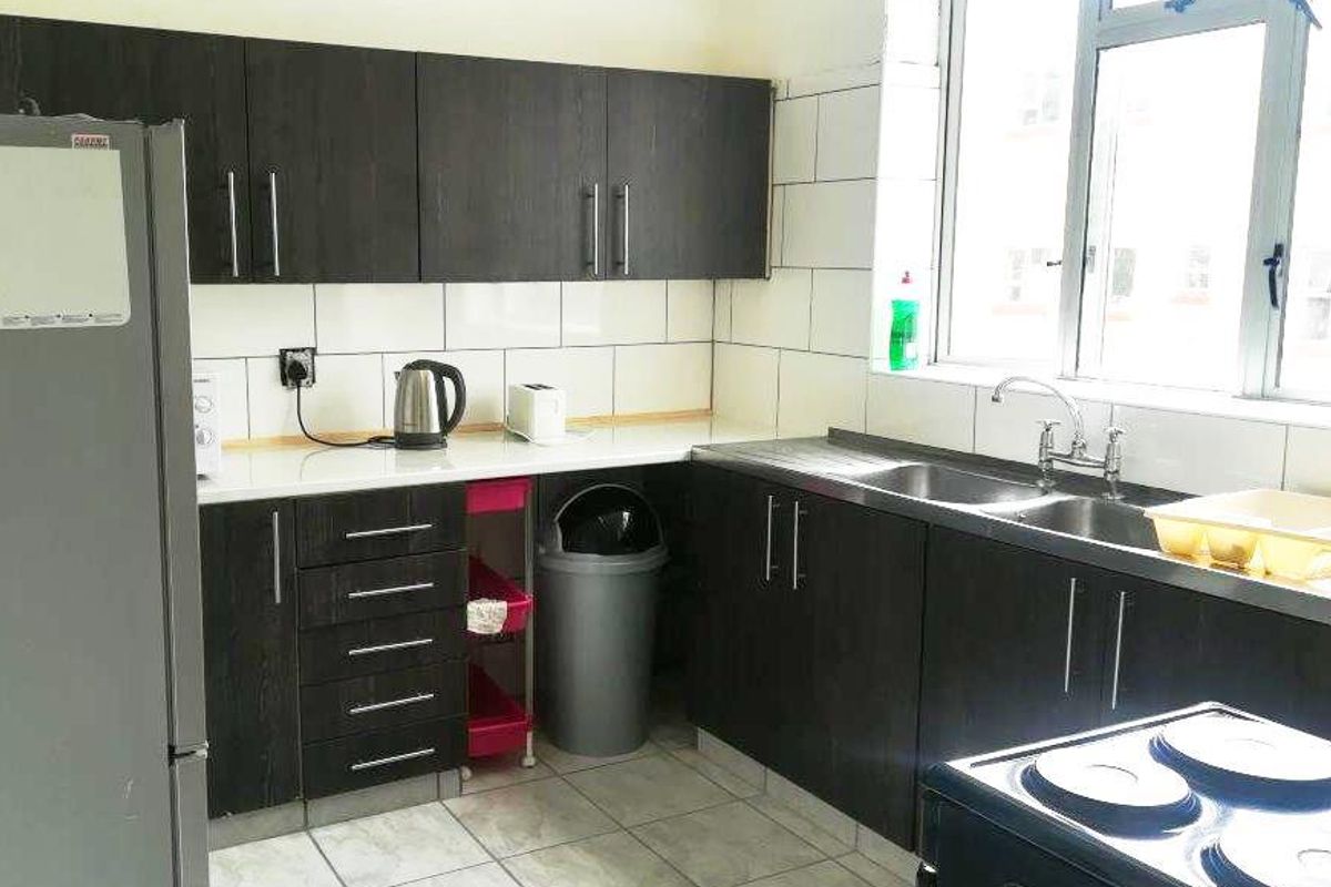 Functional kitchen featuring dark wood cabinetry, double basin sink, tiled splashback, and tiled flooring with natural light from a large window.