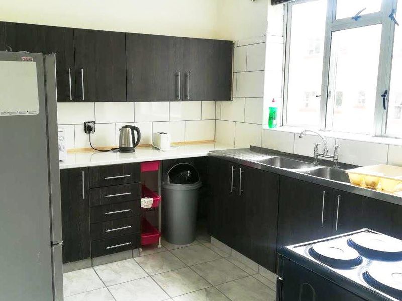 Functional kitchen featuring dark wood cabinetry, double basin sink, tiled splashback, and tiled flooring with natural light from a large window.