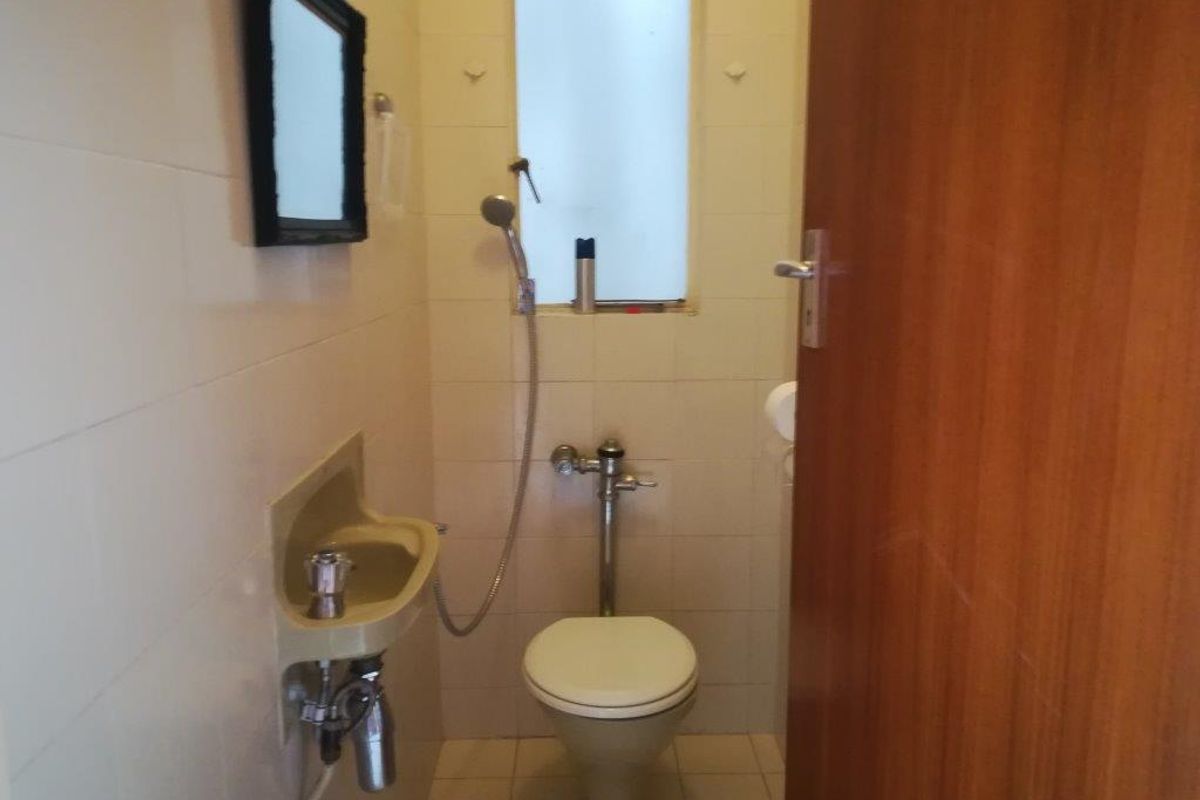 A compact, dated bathroom featuring a wall-mounted basin, toilet, and handheld shower fixture with tiled finishes.