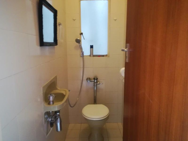 A compact, dated bathroom featuring a wall-mounted basin, toilet, and handheld shower fixture with tiled finishes.