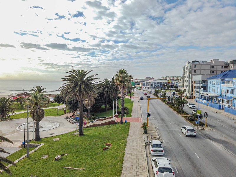 An elevated view overlooking a coastal road, public park area, and the ocean horizon under a partly cloudy sky.