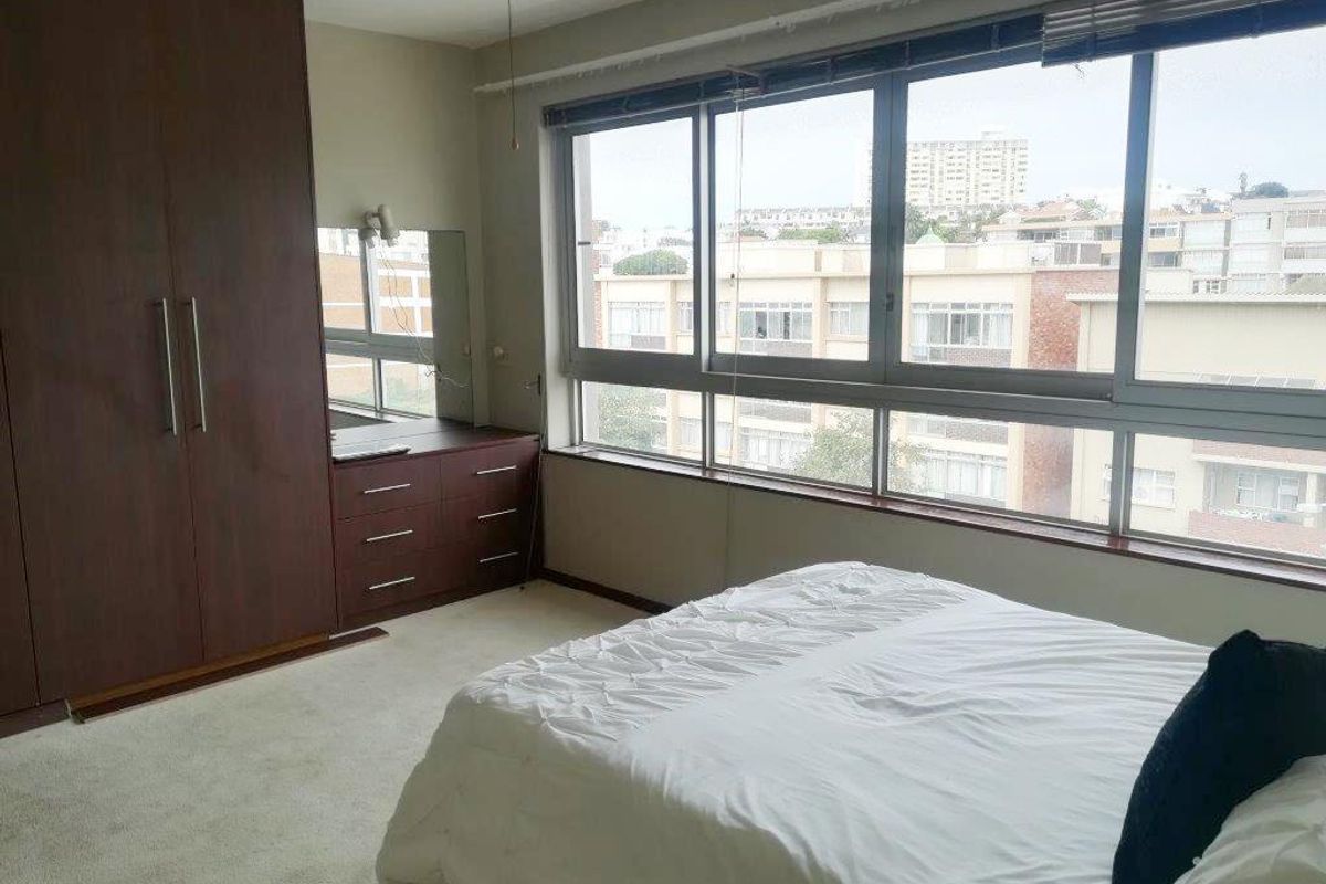 A bedroom featuring built-in dark wood cabinetry, a vanity unit, and large windows providing natural light and an urban view.