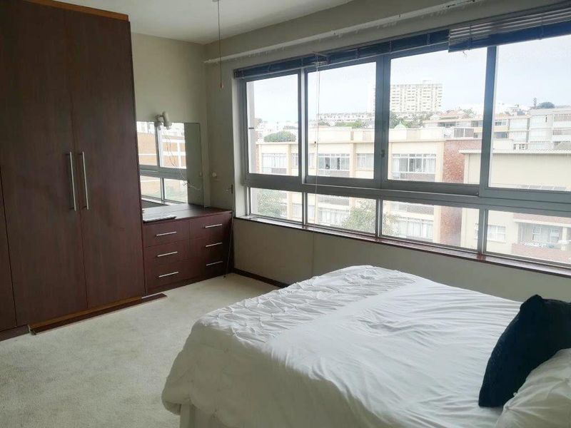 A bedroom featuring built-in dark wood cabinetry, a vanity unit, and large windows providing natural light and an urban view.