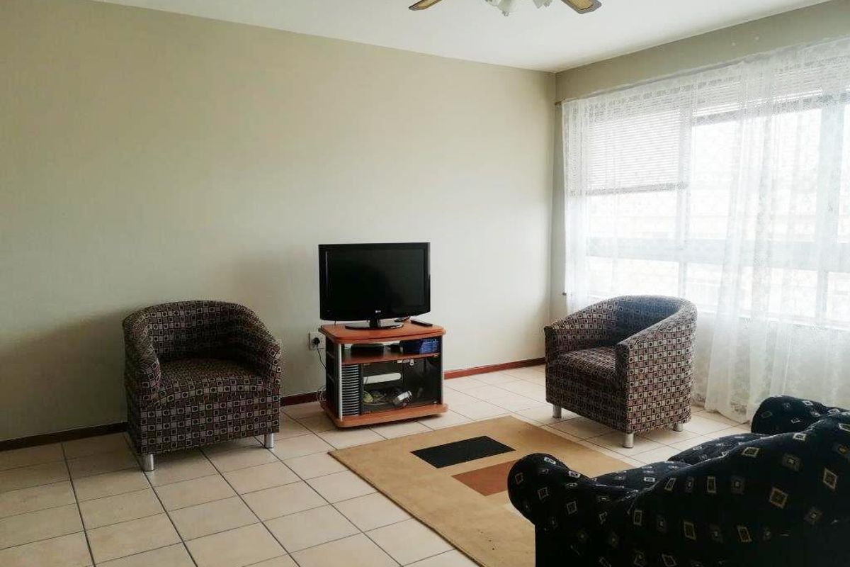 A living room featuring tiled flooring, a ceiling fan, and a large window that provides natural light.