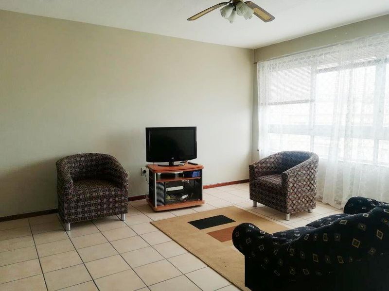 A living room featuring tiled flooring, a ceiling fan, and a large window that provides natural light.