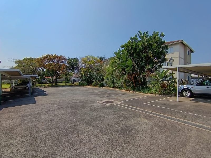 An outdoor parking area featuring asphalt surfacing, covered carport structures, and established garden landscaping within the apartment complex.