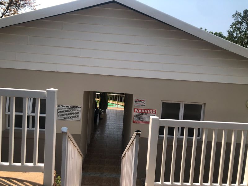 Exterior view of a clubhouse entrance featuring a tiled walkway, white picket railings, and gable roof architecture.