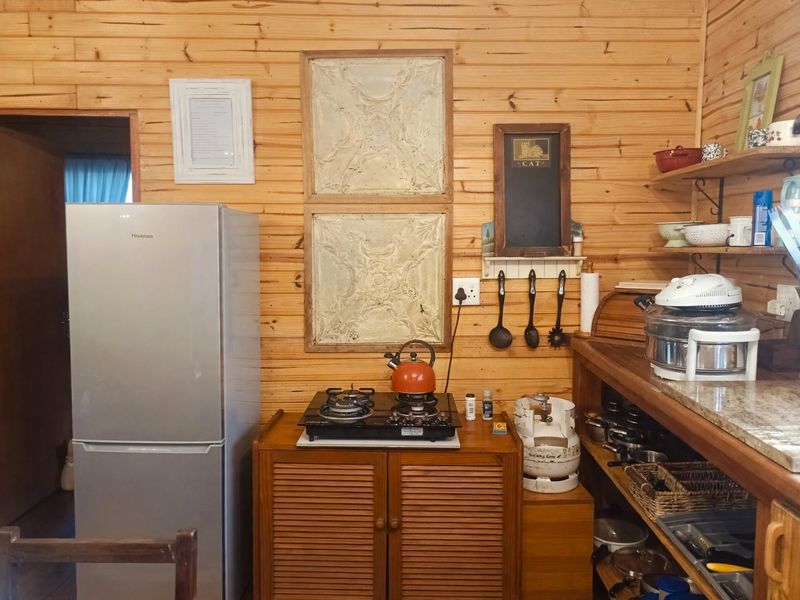 A rustic kitchen area featuring timber wall cladding, stone countertops, open shelving, and a gas cooktop setup.