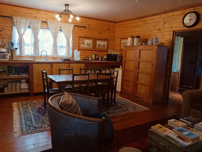 Open plan living and kitchen area featuring warm timber wall cladding, wooden flooring, and rustic cabinetry with integrated sink and dining space.