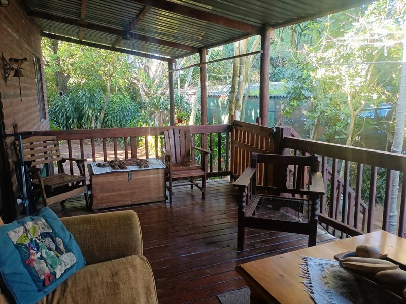 A covered timber deck patio featuring wooden balustrades and a corrugated metal roof, overlooking a lush garden setting.