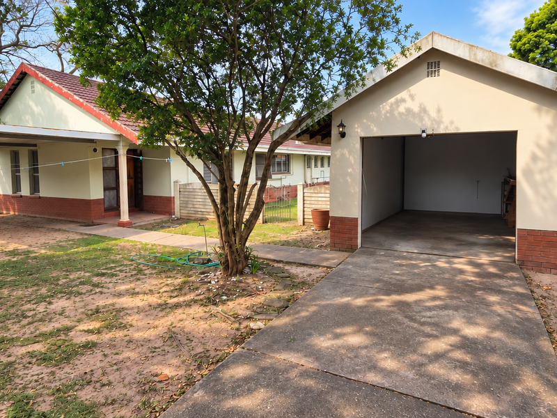 Front view of the property featuring a detached garage, a carport, a concrete driveway, and a garden area with established trees.