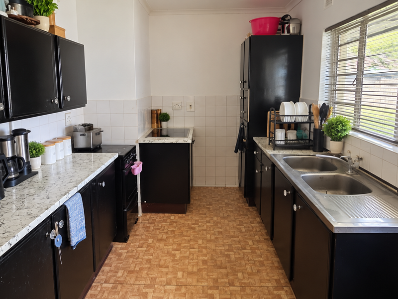 A functional kitchen featuring black cabinetry, laminate countertops, a double bowl stainless steel sink, and a tiled backsplash with a window view.