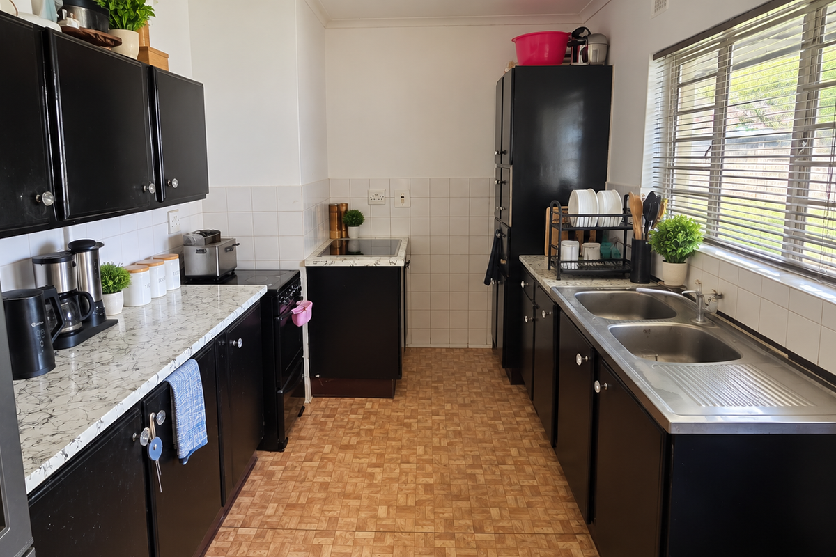 A functional kitchen featuring black cabinetry, laminate countertops, a double bowl stainless steel sink, and a tiled backsplash with a window view.