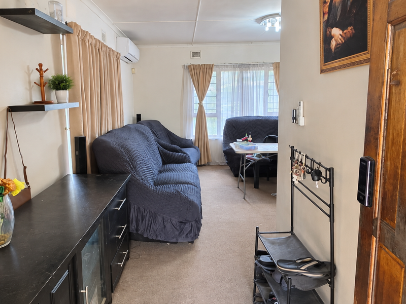 A living room area featuring carpet flooring, an air conditioning unit, and a decorative timber entrance door.