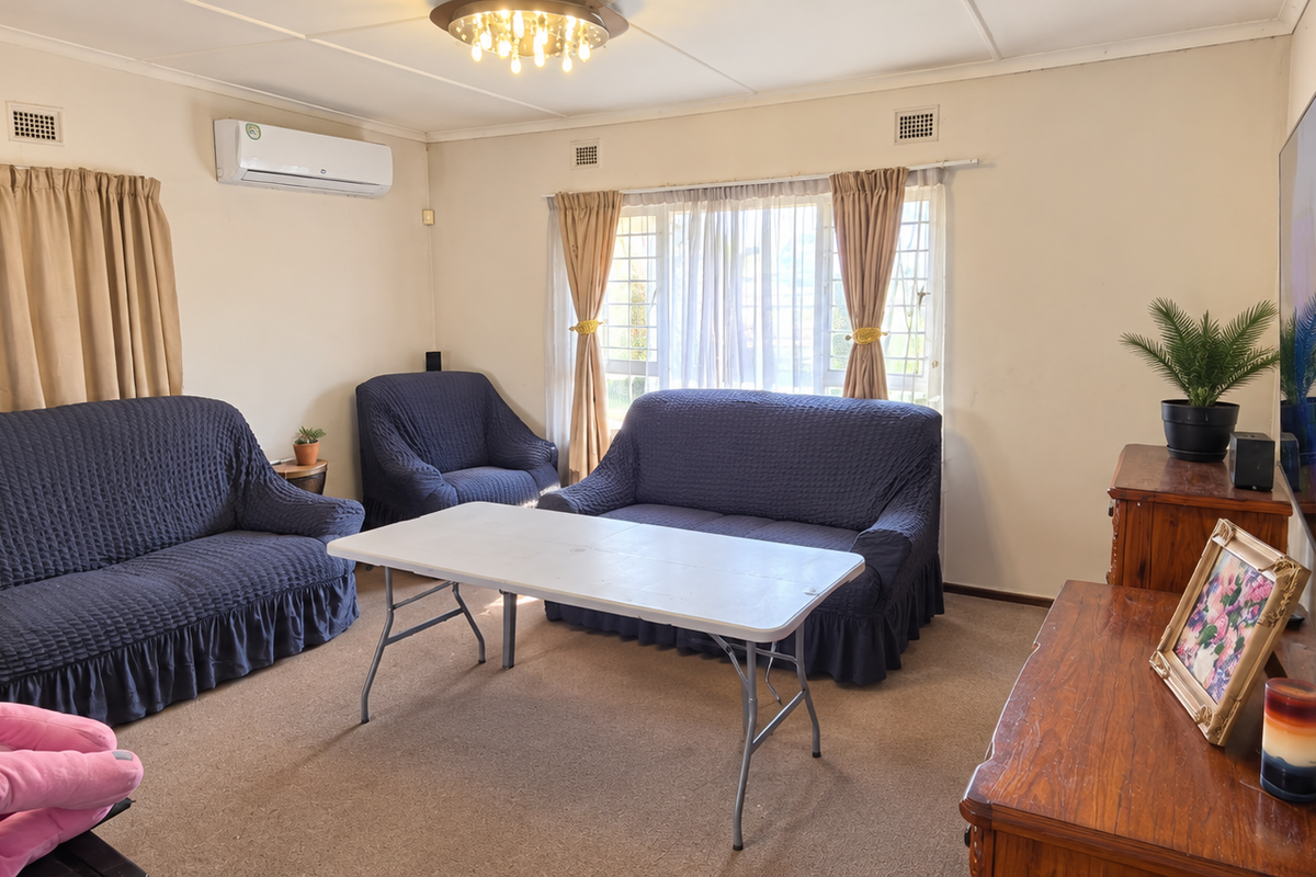 A comfortable living room featuring a wall-mounted air conditioning unit, carpeted flooring, and large windows with security bars.