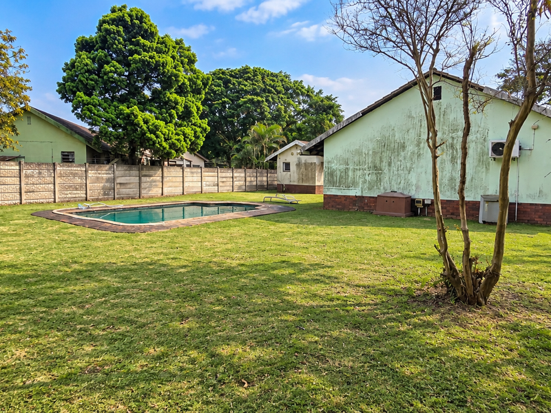 Spacious rear garden featuring a swimming pool, expansive lawn, and perimeter boundary wall, with visible maintenance required on the exterior building facade.