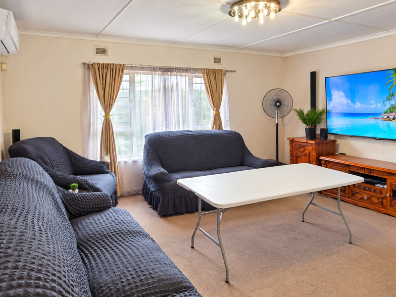 A spacious living room featuring neutral wall finishes, carpeted flooring, and an installed air conditioning unit.