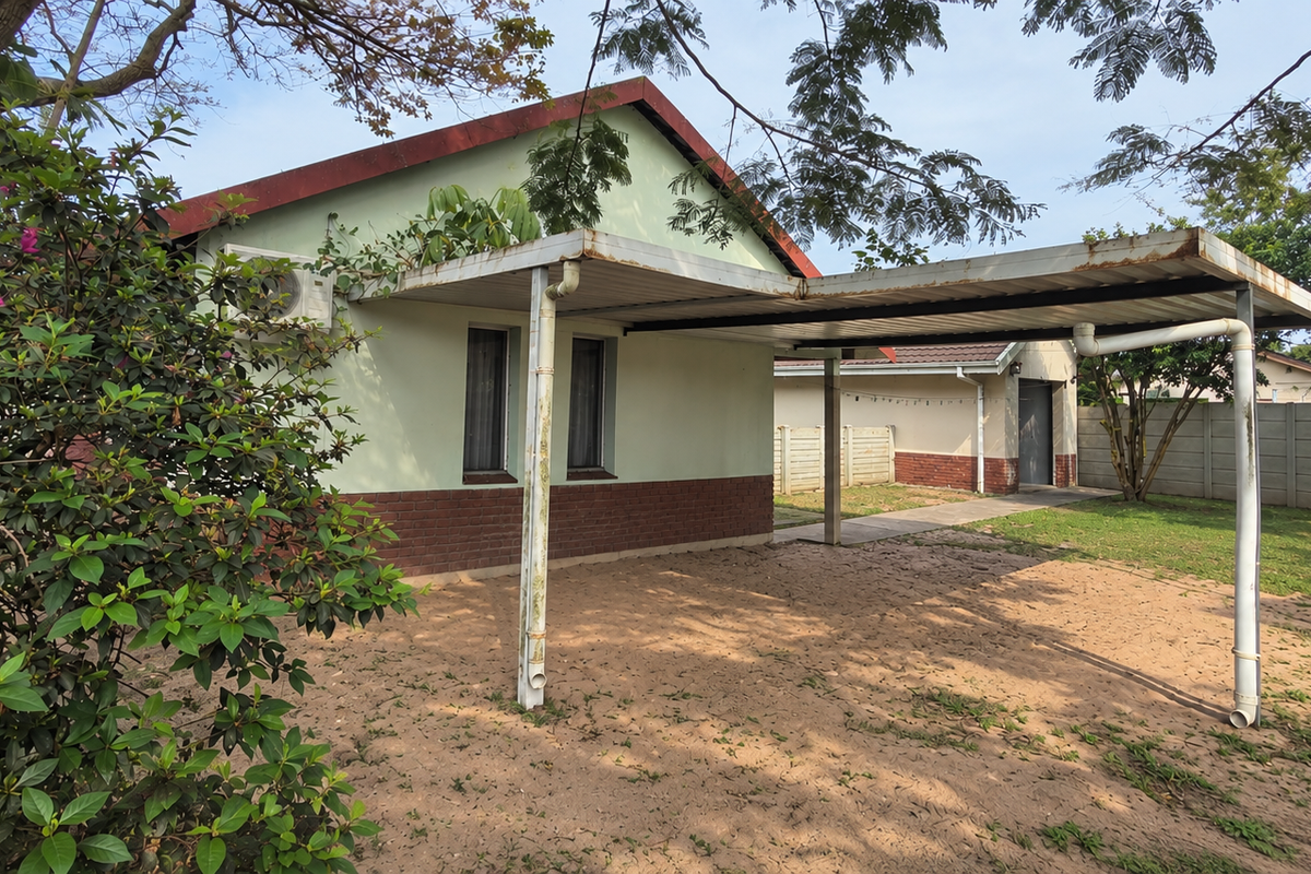 Rear exterior view of the property featuring a metal carport, brick-base facade, and a concrete boundary wall in a garden setting.