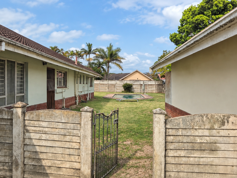 Rear view of the property featuring a swimming pool, lawn area, and precast concrete boundary walls between two building structures.