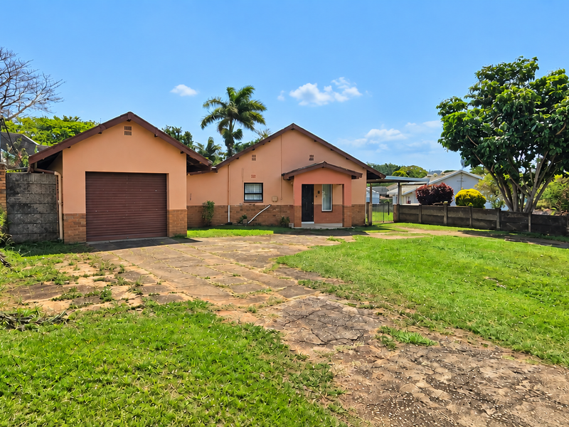 Front view of a detached house featuring a single garage, paved driveway, and established garden with boundary walling.