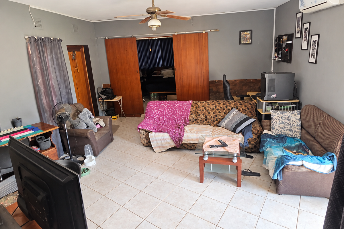 A spacious living room featuring tiled flooring, a ceiling fan, and sliding wooden doors leading to an adjacent area, equipped with an air conditioning unit.