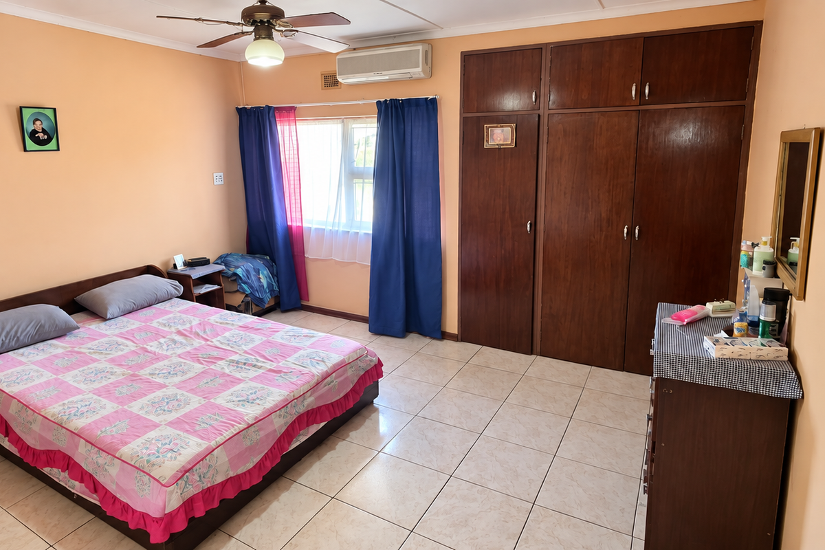 A spacious bedroom featuring tiled flooring, built-in wooden cupboards, a ceiling fan, and a wall-mounted air conditioning unit.