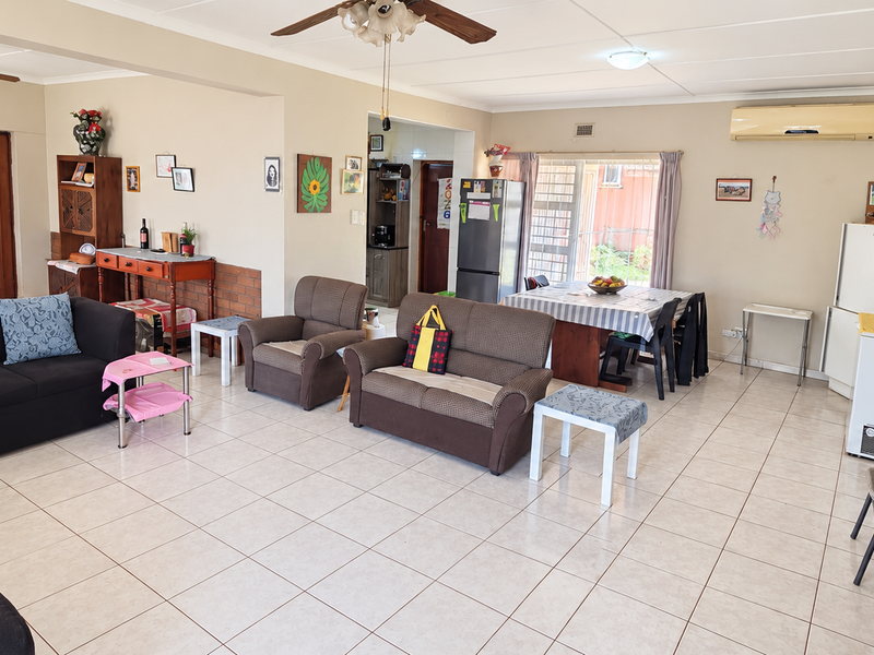 Spacious open-plan living and dining area featuring tiled flooring, ceiling fans, and a wall-mounted air conditioning unit.