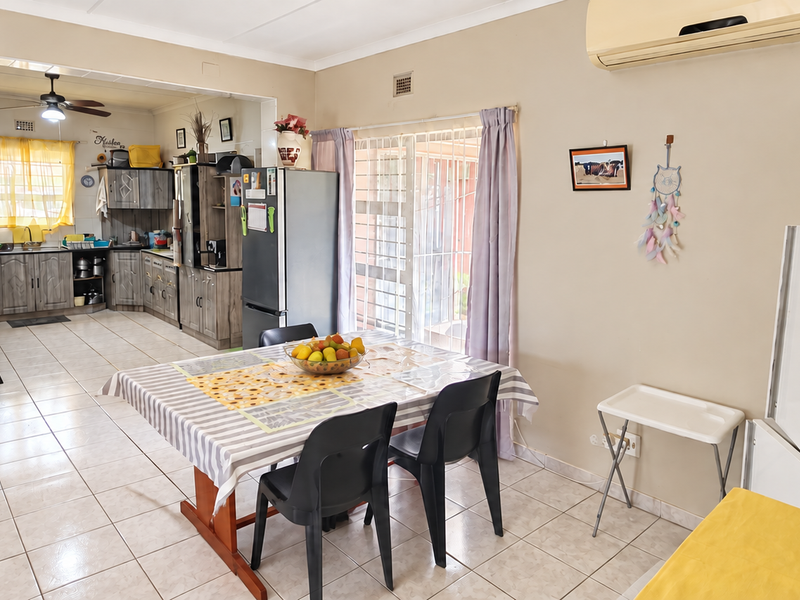 Open-plan living and dining area flowing into a functional kitchen with tiled flooring and a wall-mounted air conditioning unit.