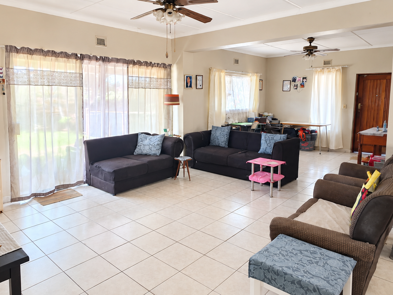 Spacious open-plan living area featuring neutral tiled flooring, ceiling fans, and large sliding glass doors providing natural light and garden access.