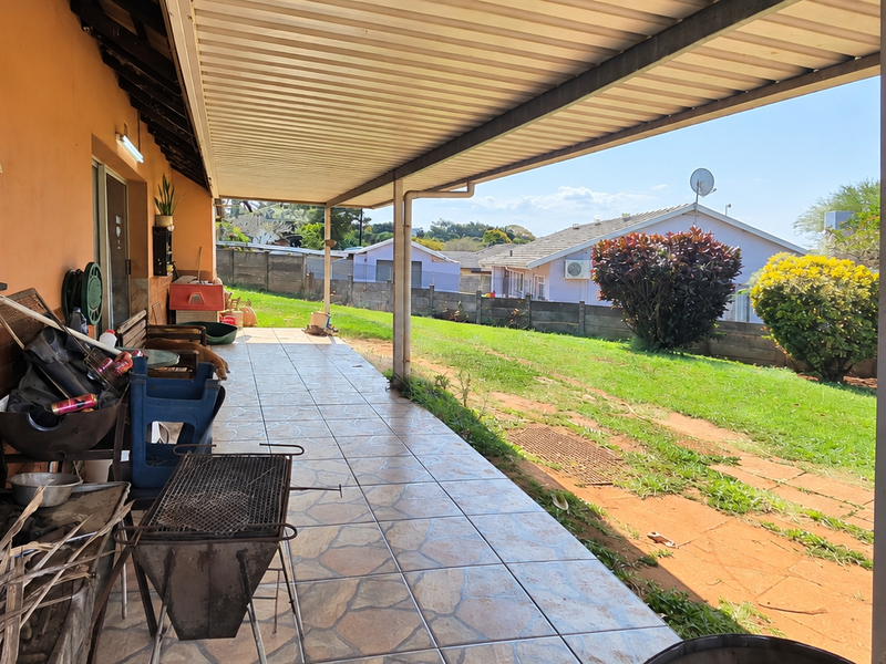 A covered outdoor patio area featuring tiled flooring, brick wall accents, and direct access to the rear garden space.