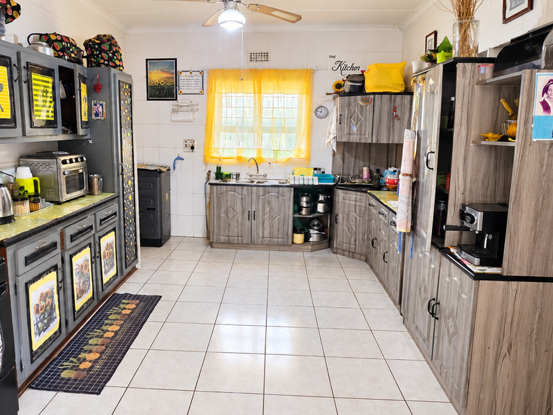 A functional kitchen featuring tiled walls and flooring, ample built-in cabinetry, a gas stove, and a double sink with a window view.