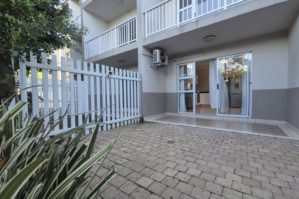 A private ground floor patio area featuring paved flooring, a white picket fence, and direct access to the apartment interior via sliding glass doors.