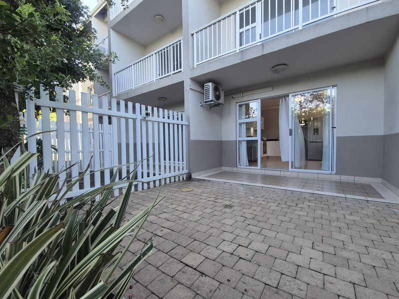 A private ground floor patio area featuring paved flooring, a white picket fence, and direct access to the apartment interior via sliding glass doors.