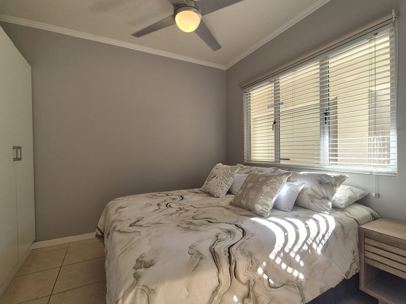 A well-maintained bedroom featuring tiled flooring, a ceiling fan, built-in wardrobe, and venetian blinds allowing natural light.