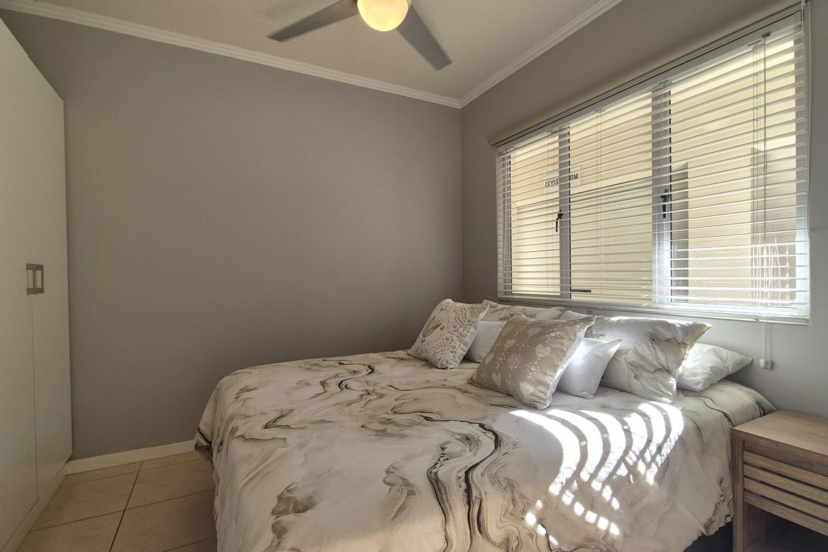 A well-maintained bedroom featuring tiled flooring, a ceiling fan, built-in wardrobe, and venetian blinds allowing natural light.