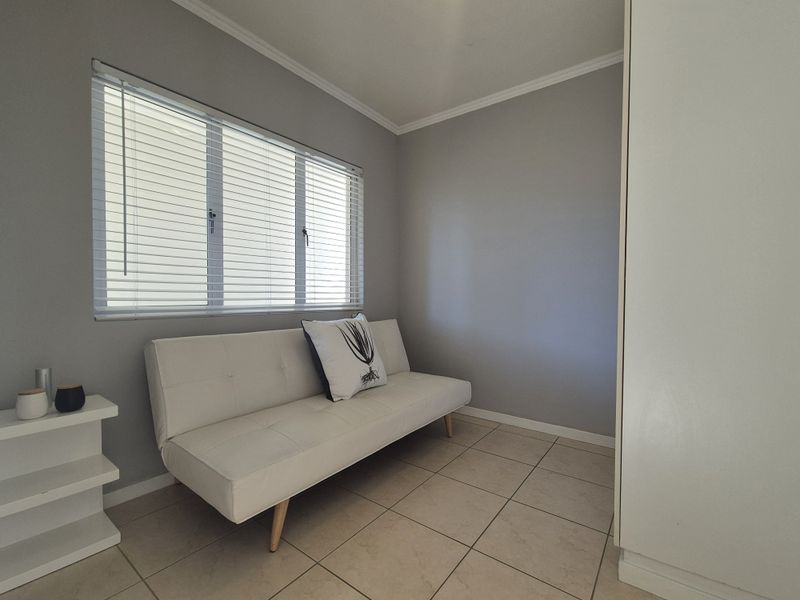 A compact bedroom featuring neutral grey walls, tiled flooring, built-in storage, and venetian blinds for natural light control.