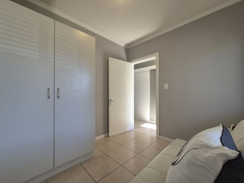 A bedroom featuring tiled flooring, built-in wardrobe storage, and neutral wall finishes, with a doorway leading to an adjacent hallway.
