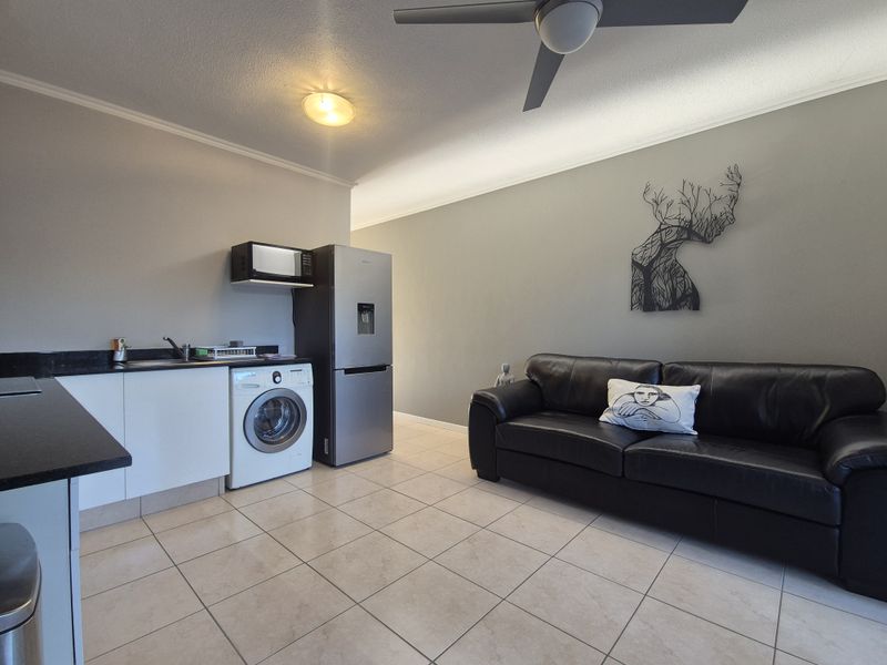 Open-plan living area featuring tiled flooring, a compact kitchen kitchenette with built-in cabinetry, and a ceiling fan for climate control.