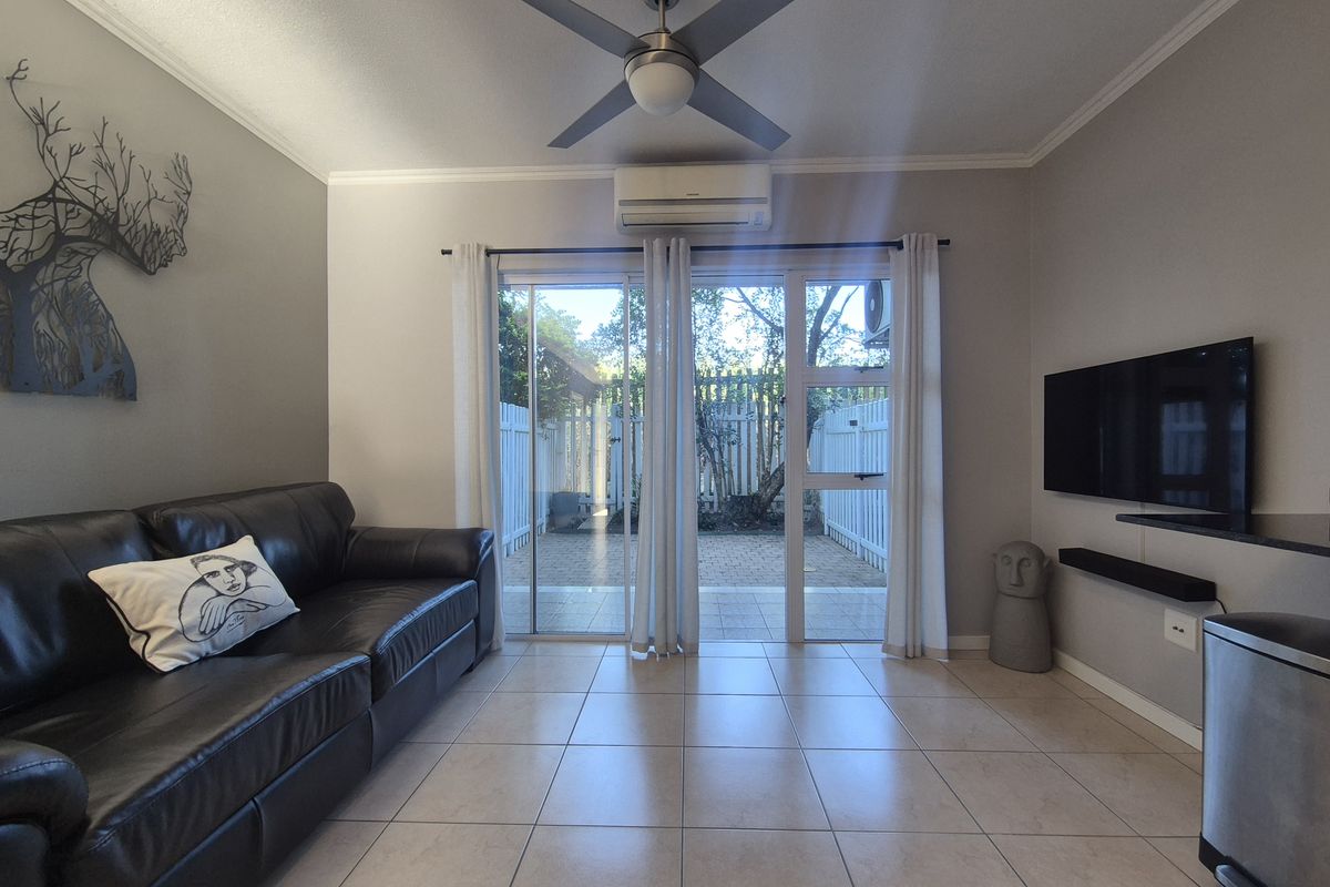 A well-maintained living room featuring tiled floors, a ceiling fan, split-system air conditioning, and sliding glass doors providing access to a private outdoor area.