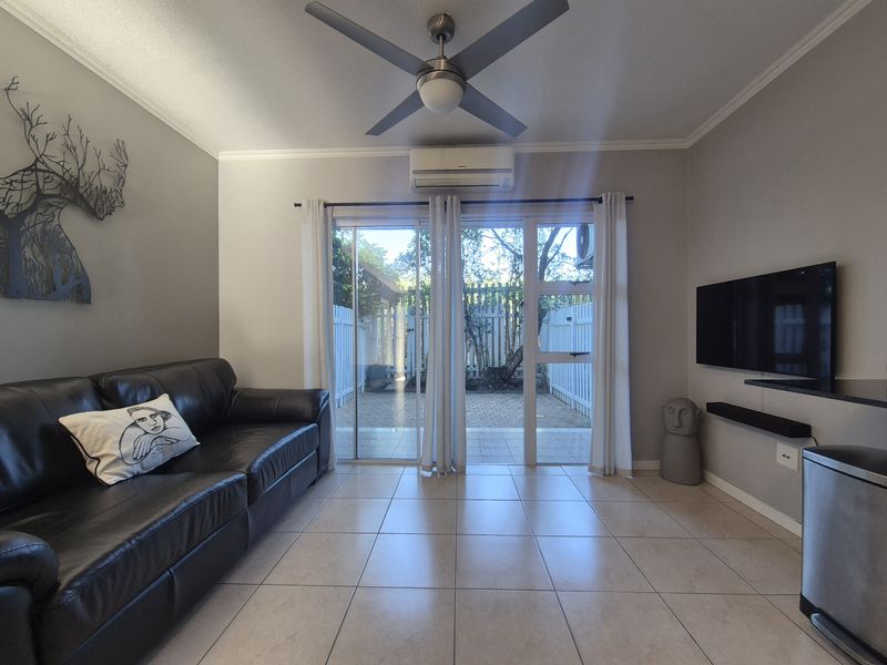 A well-maintained living room featuring tiled floors, a ceiling fan, split-system air conditioning, and sliding glass doors providing access to a private outdoor area.