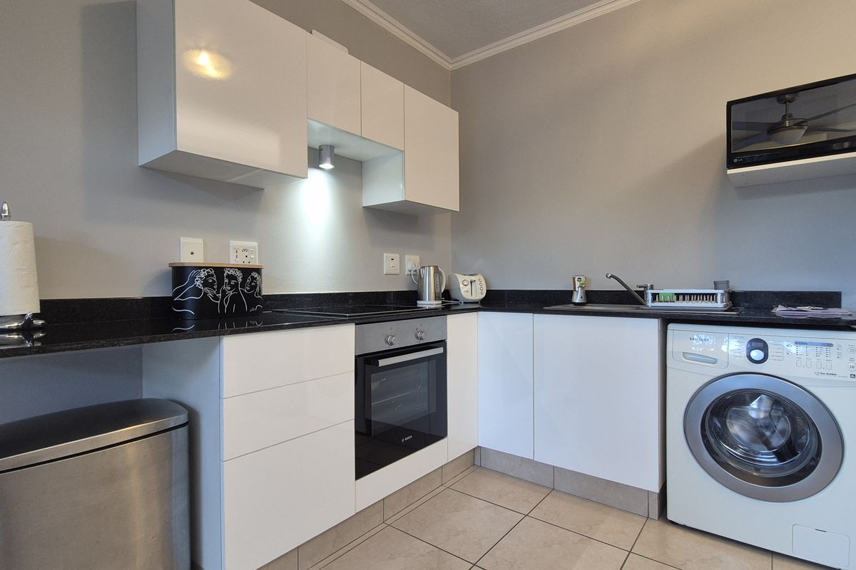 Modern kitchen featuring white high-gloss cabinetry, black granite countertops, integrated oven and hob, and dedicated space for a washing machine.