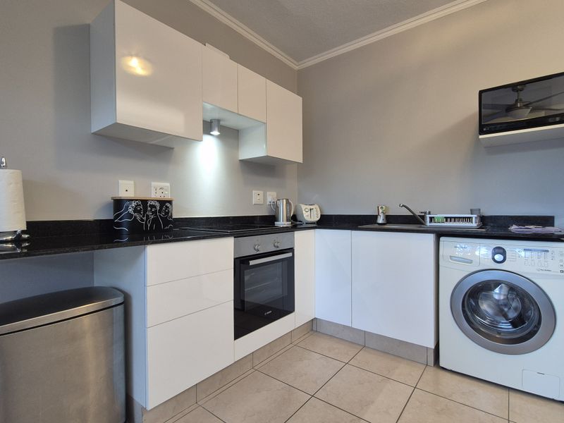 Modern kitchen featuring white high-gloss cabinetry, black granite countertops, integrated oven and hob, and dedicated space for a washing machine.