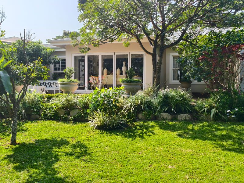 A well-maintained rear garden featuring a lush lawn, mature trees, stone landscaping, and large bi-fold doors leading into the home.