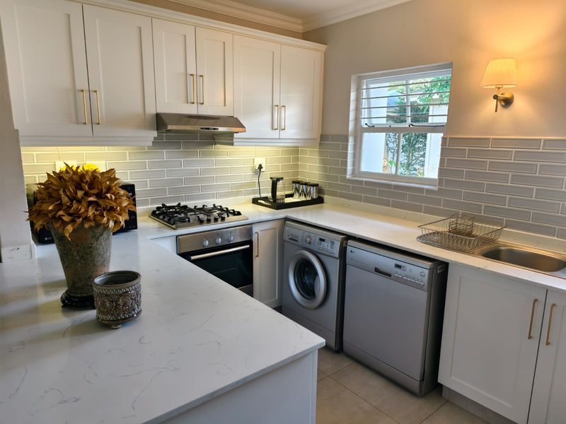 Modern kitchen featuring white shaker-style cabinetry, stone countertops, subway tile backsplash, integrated gas hob, oven, and under-cabinet lighting.